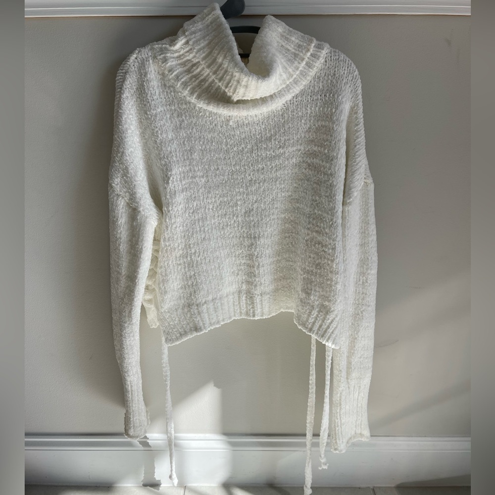 White loose turtleneck sweater, lightly worn with side tie ups.